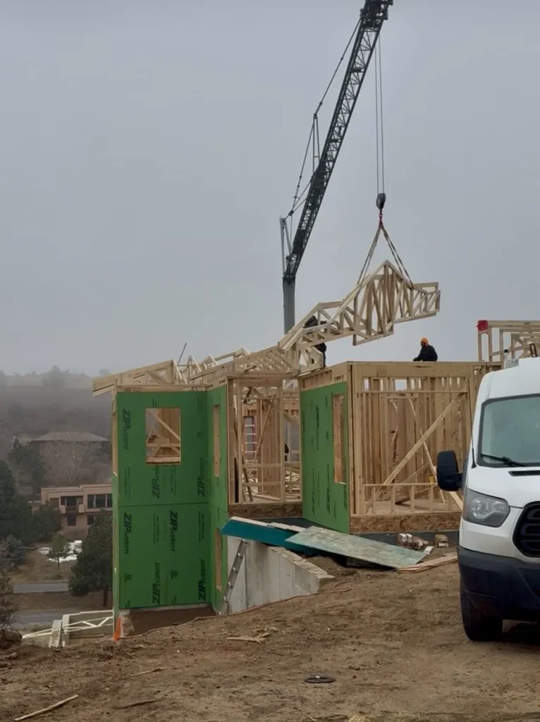 Crane placing wooden roof trusses on a new custom home under construction in Denver, built by Camerata Homes